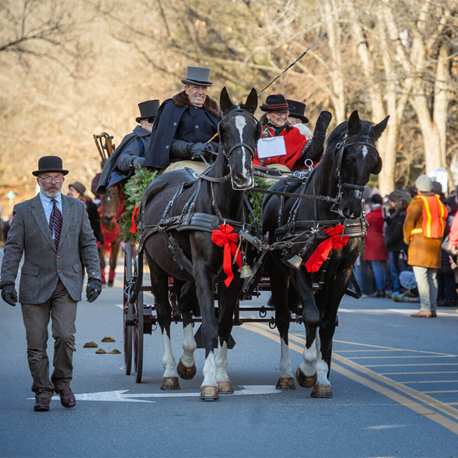People in holiday clothes in a horse-drawn carriage in the winter waving at a gathered crowd.&nbsp;