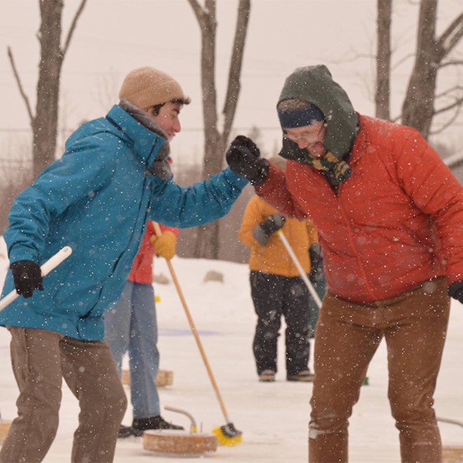  People dressed for winter weather shake hands on a lake during a curling match as snow falls.&nbsp;