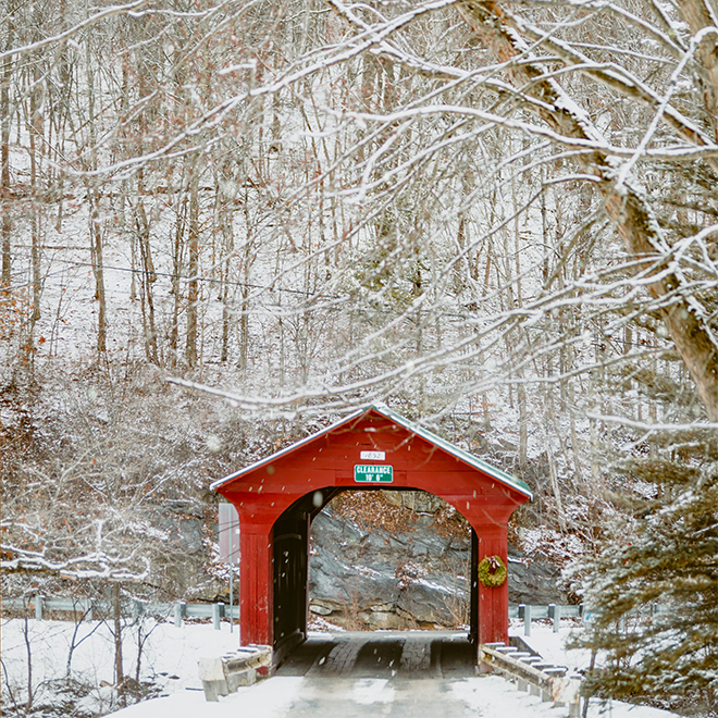 A red covered bridge on a snowy winter day with snow falling around.&nbsp;