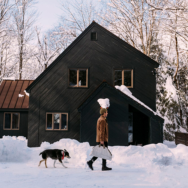 A person carries firewood in front of a house followed by a dog.&nbsp;