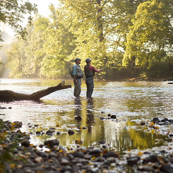 Two people seen from a distance fly fishing in a rushing river.&nbsp;