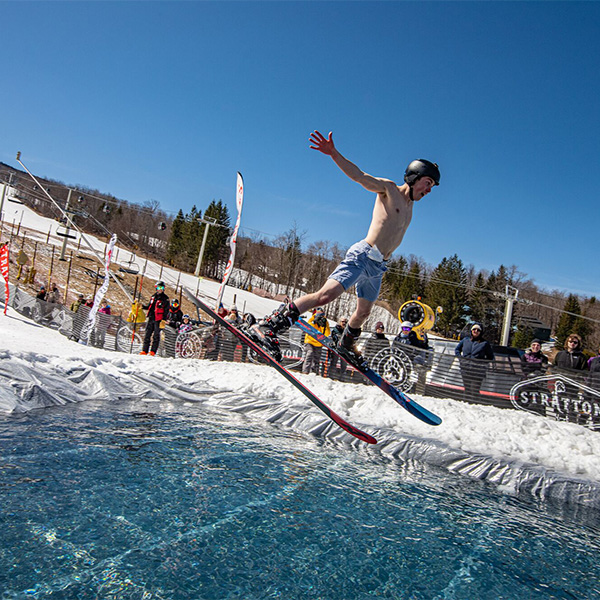 A person on skis attempts to skim over a man-made pond at a resort while others cheer and watch.  