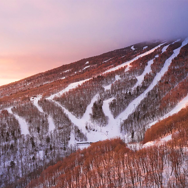 A ski area seen from above in warm spring light with snow visible on trails.