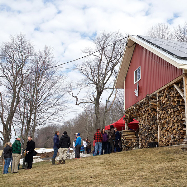 People seen outside a sugarhouse in the spring with steam coming from the roof.&nbsp;