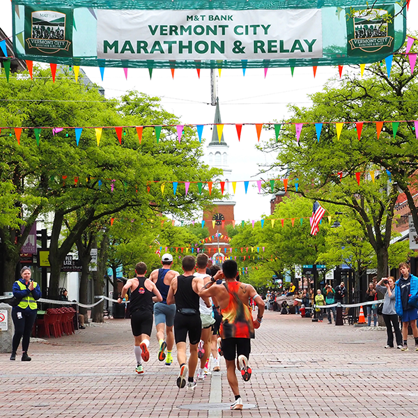 Runners on a summer street under a banner advertising a marathon event.&nbsp;