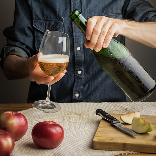  A person pours an amber-colored cider into a wine glass at a table at an event. 