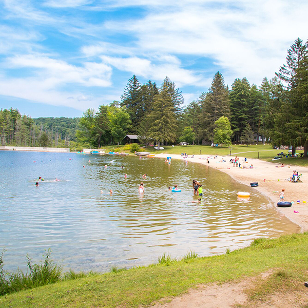 A sandy beach on the shore of a lake. Some people are in the water while others relax on the beach on a sunny day.