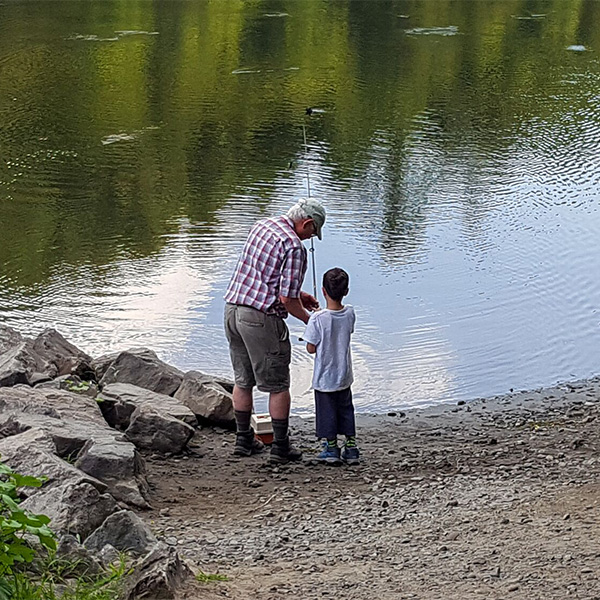 Two people at the shore of a river fishing together. 