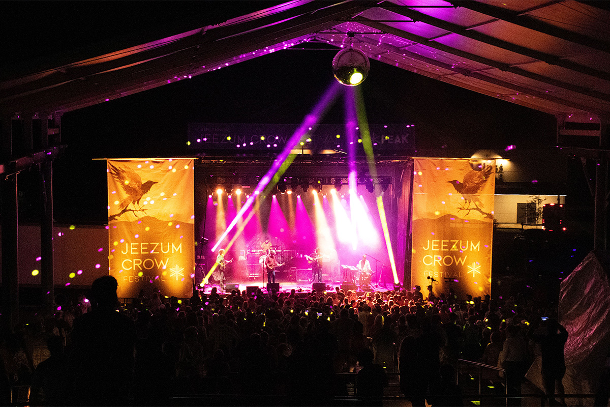 A live music show at night with brightly colored lights casting beams over a stage and people gathered to hear the music.&nbsp;