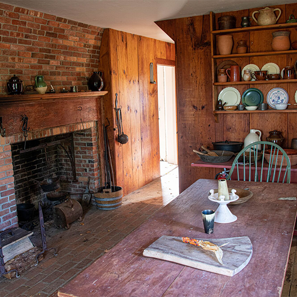 The inside of a historic homestead with wooden furniture and historic kitchen tools visible.&nbsp;