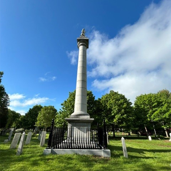 A tall monument seen outside on a sunny summer day. Beside it are several other stone memorials.