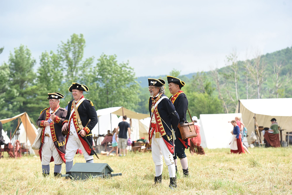 People in historic costumes re-enact a Civil War scene outside in the summer at a historic site. 