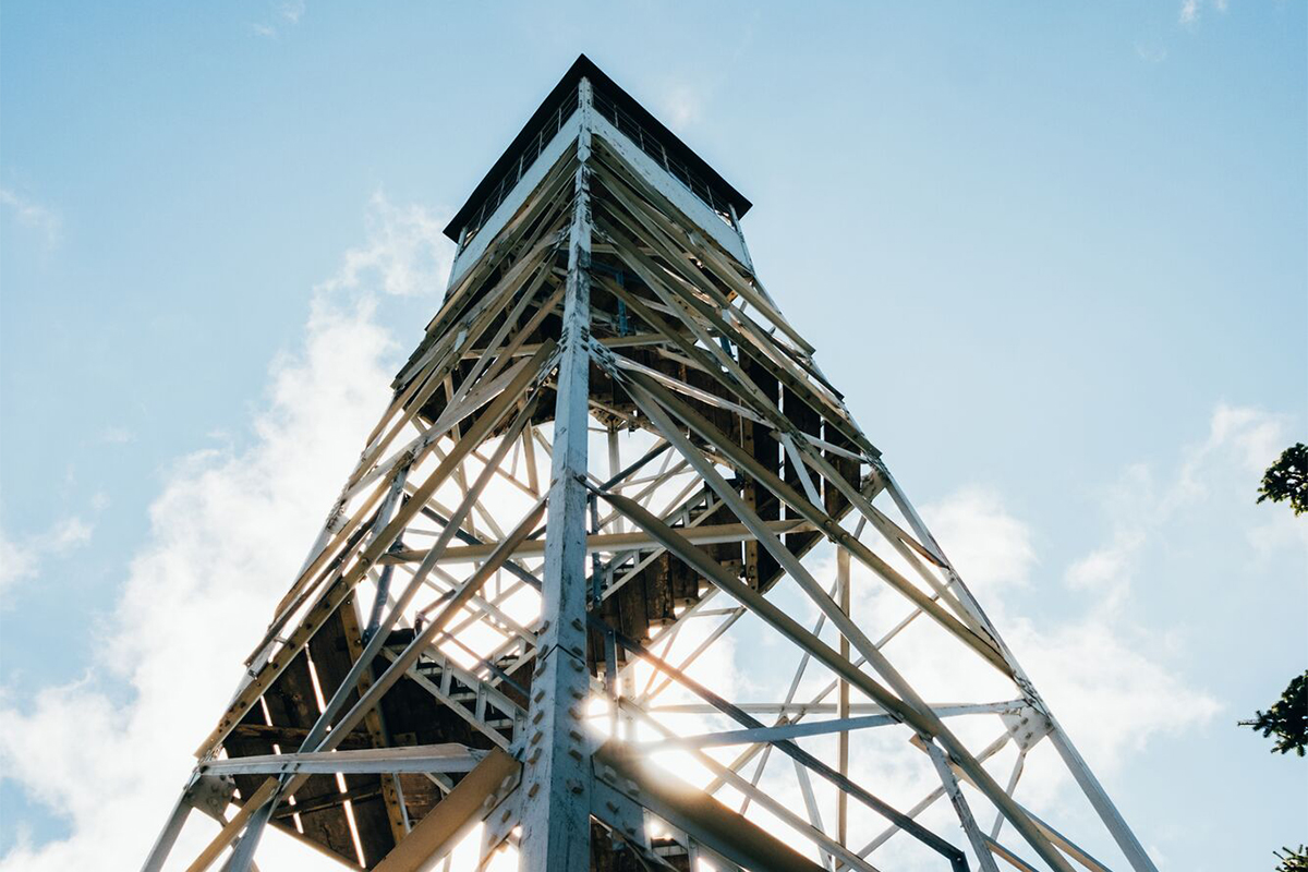 Seen from below, a fire tower stretches up into the sky on a sunny summer day. 