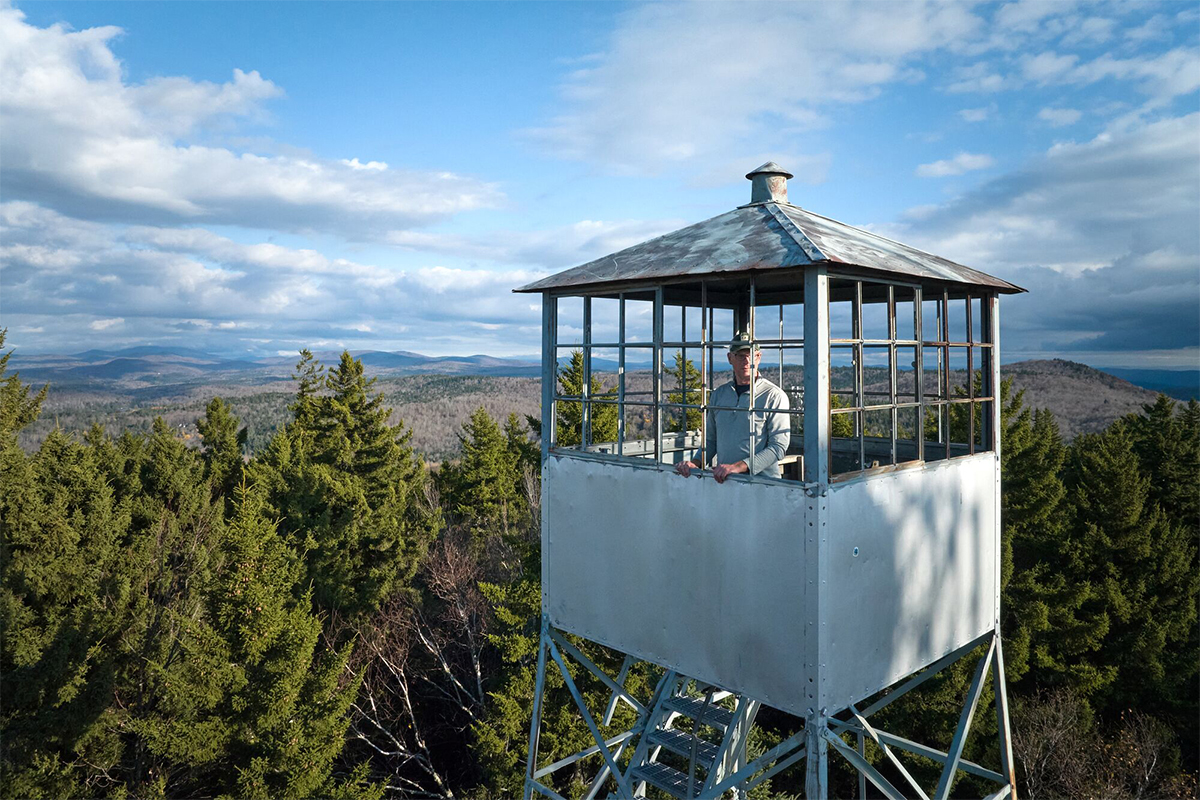 A fire tower with a person inside enjoying the view, seen from above on a sunny summer day. 