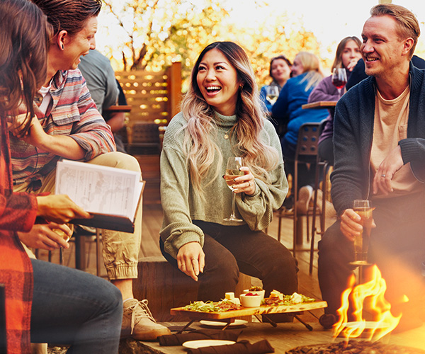 Friends chatting in front of a fire, enjoying drinks and appetizers.