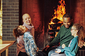 A family laughing and staying warm in front of a fire.