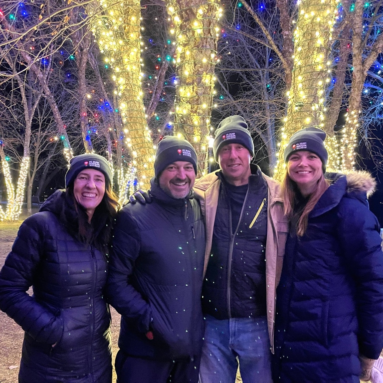 Friends standing in front of trees lit up with christmas lights