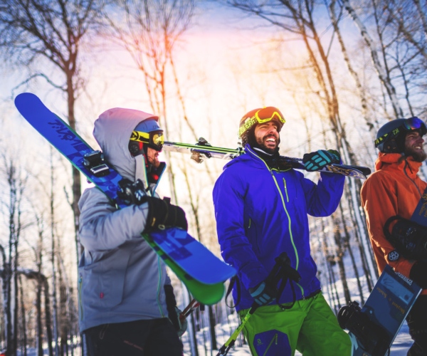 friends carrying skis and snowboard on ski hill 