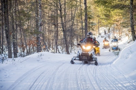 family snowmobiling in the woods along a snowmobile trail