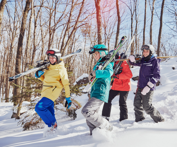 friends carrying downhill skis while walking through the woods