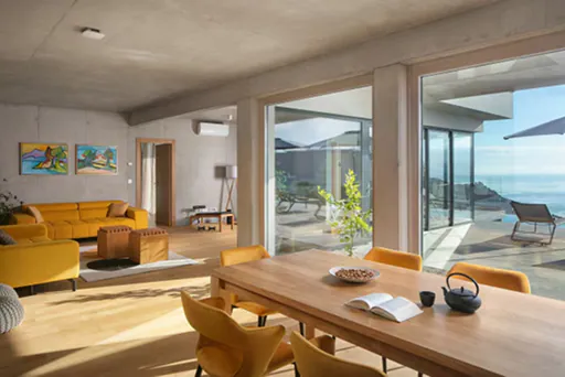 A gorgeous vacation home decorated in warm tones with floor-to-ceiling windows looking out over the sea