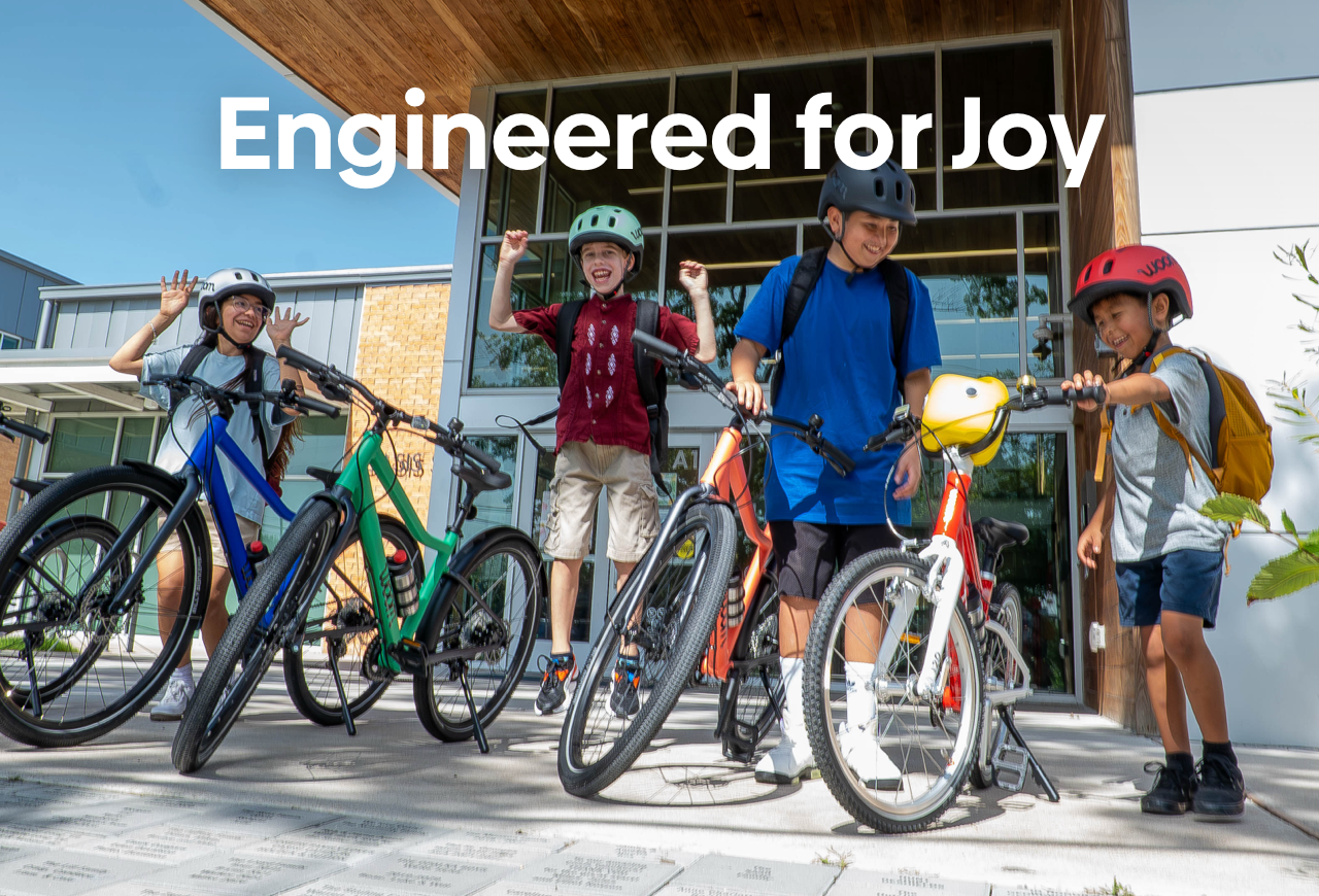 A collection of woom GO and EXPLORE bikes with their riders in front of a school