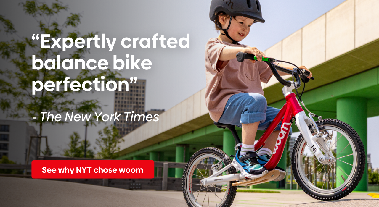 Young boy in a black READY Helmet on a woom GO 1 rides next to a New York Times quote: "Expertly crafted balance bike perfection"