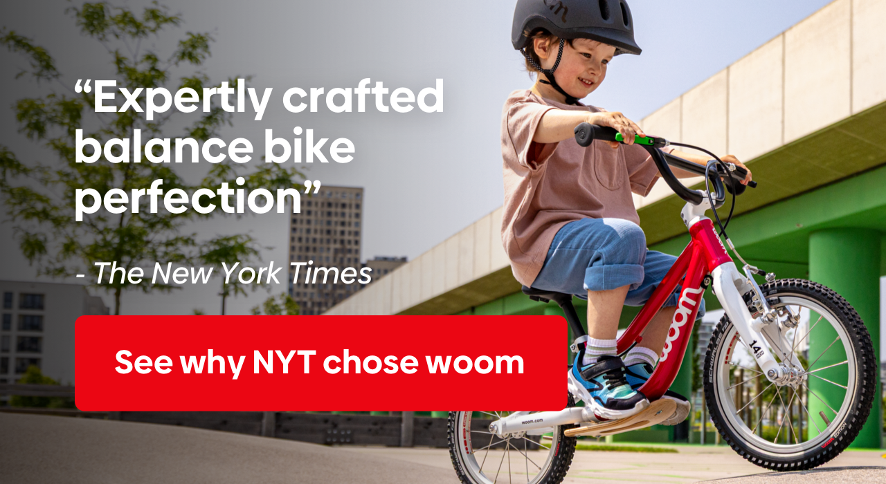Young boy in a black READY Helmet on a woom GO 1 rides next to a New York Times quote: "Expertly crafted balance bike perfection"
