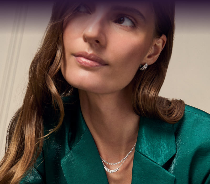 A model wearing gold gemstone hoops, a charm necklace and diamond rings. Gifts for her. Click here to shop now