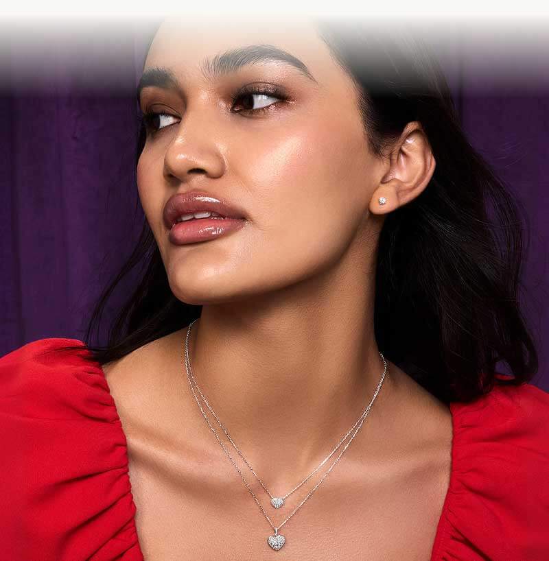 Model in red top, with two diamond heart necklaces and diamond studs.