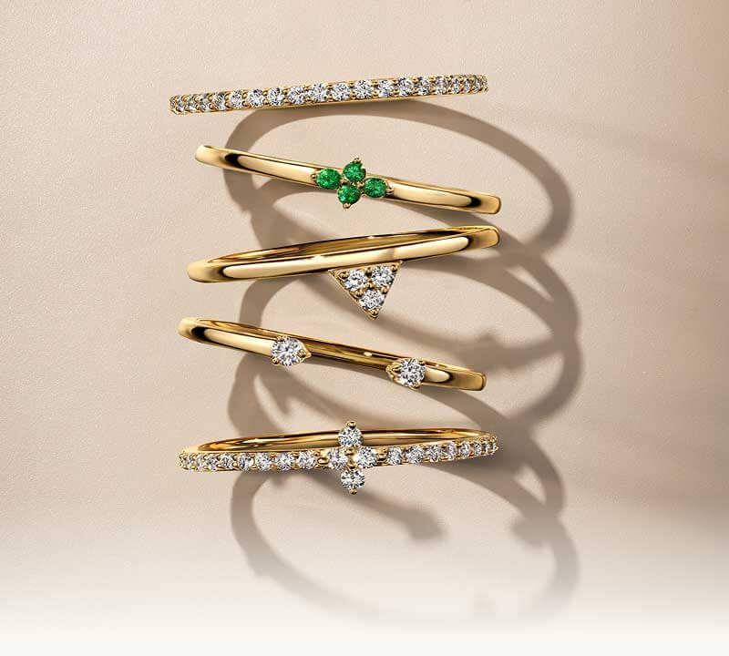 A lineup of gold stacked rings with diverse diamond details, and emerald gemstones.