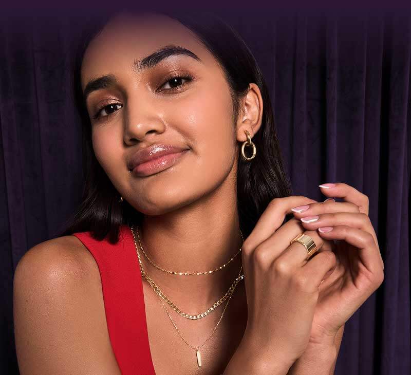 Model wearing gold chain necklaces, hoops and ring. 