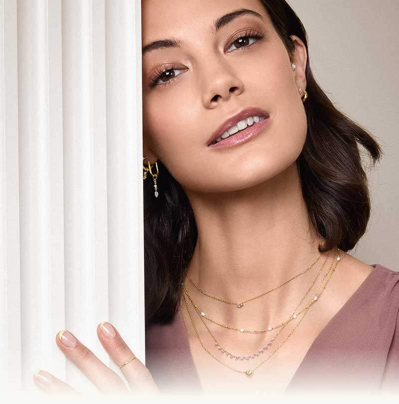 Model with unique gold ear stack & layered dainty gold necklaces with mini pendants, pink gemstones & pearls.