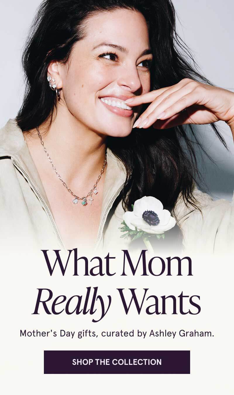 Ashley Graham holding flower in diamond studs, hoops & paper clip chain with charms. Mother’s Day Gifts, by Ashley Graham. Click here to shop the collection