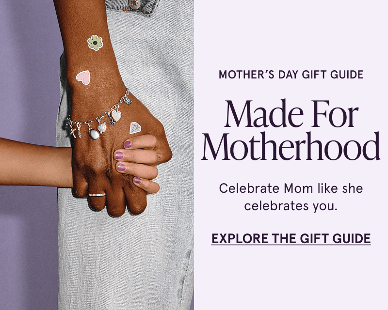 Motherhood. Celebrate Mom. Model holding child’s hand with paper clip charm bracelet & stickers. Click here to explore the gift guide