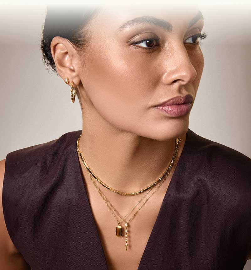 Model in gold layered chains with gemstone &  hanging pendants, with gold ear stack.